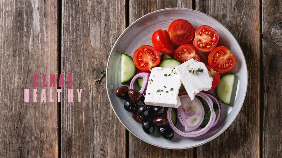 Ingredients for traditional greek salad. Cherry tomatoes, sliced cucumbers, red onion, black olives, feta cheese gray ceramic plate over wooden plank background. Top view with copy space