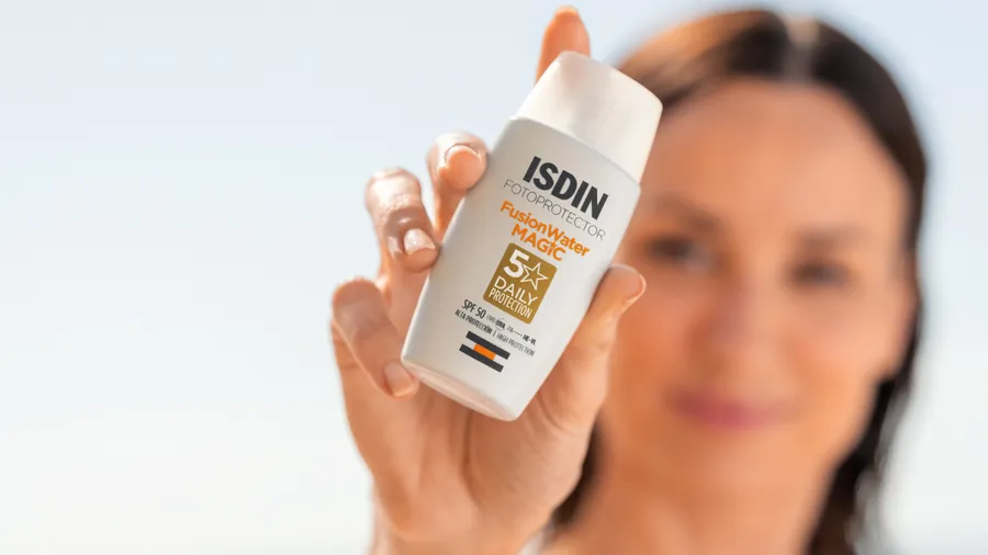 Una mujer muestra el envase del protector solar Fusion Water Magic Oil Control de la marca ISDIN