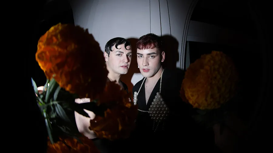 Dos visitantes de la Ofrenda de Muertos de Jean Paul Gaultier, en primer plano flores de cempasúchil.
