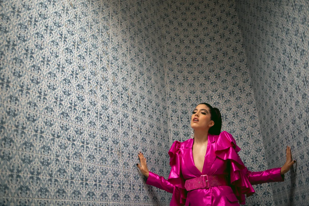 Ana riza usa un blazer rosa con cinturon gruesas y olanes en las mangas.