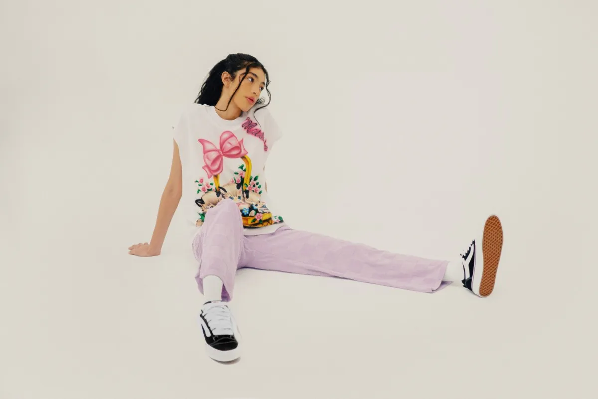 Una mujer con pants rosa, playera blanca con diseño y sneakers vans Knu Skool de Vans.