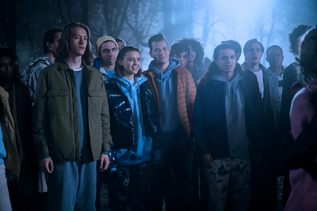 Merlina. Percy Hynes White como Xavier Thorpe, Johnna Dias-Watson como Divina, Oliver Watson como Kent.