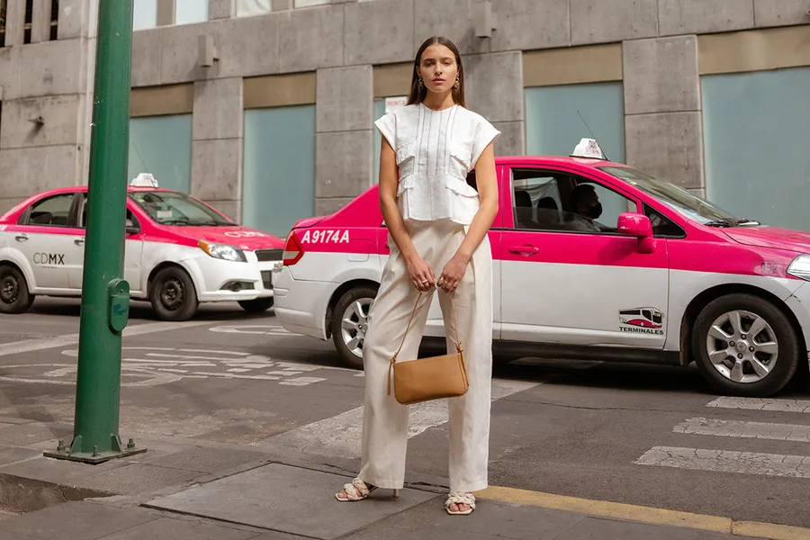 Mujer viste colección YAKMAPOT for MAP en banqueta con taxis rosas de fondo