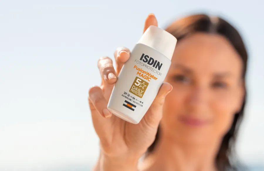 Una mujer muestra el envase del protector solar Fusion Water Magic Oil Control de la marca ISDIN