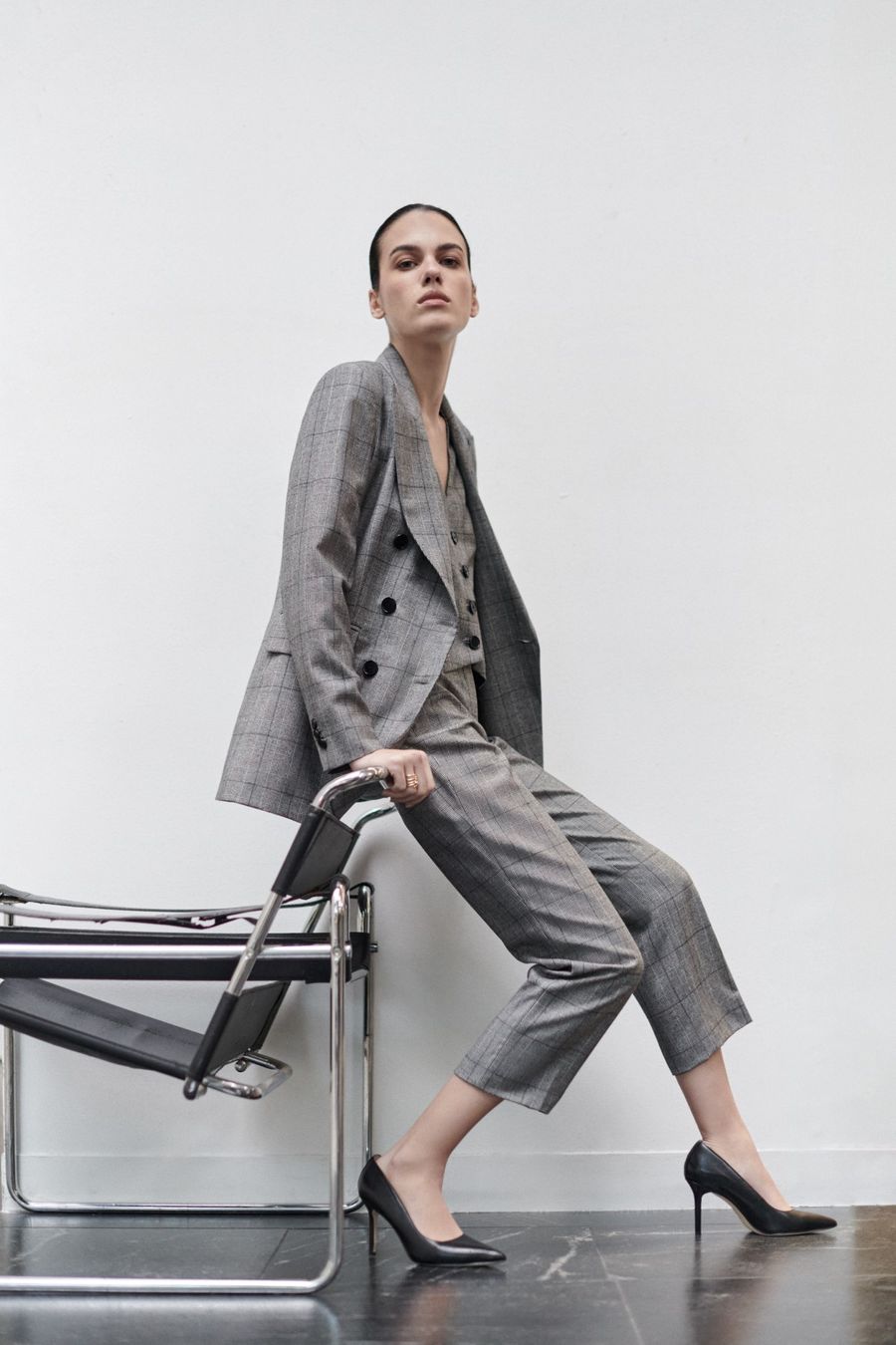 Mujer vestida con pantalón y saco grises posa en una oficina, con ropa de la marca DHierro de El Palacio de Hierro